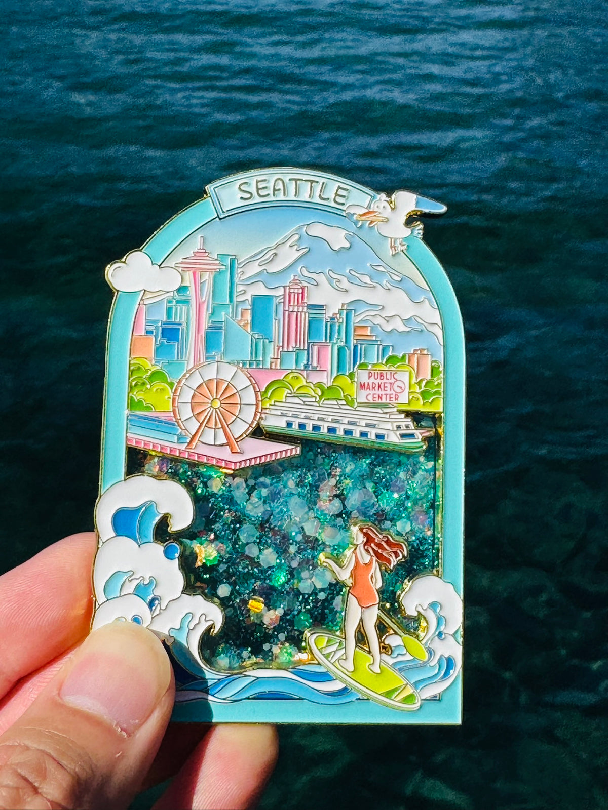 Decorative pin with Seattle-themed design held over water
